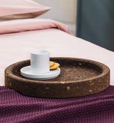 a cup and saucer sitting on top of a bed next to a pink blanket