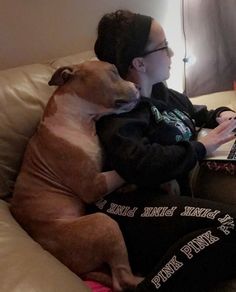 a person sitting on a couch with a dog using a laptop