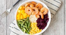 a white bowl filled with shrimp, rice and veggies next to a fork