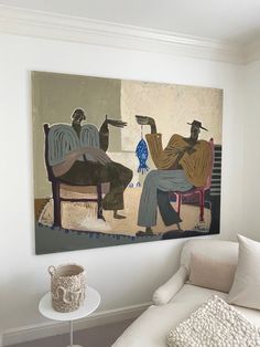 a painting hanging on the wall above a white couch in a room with two people