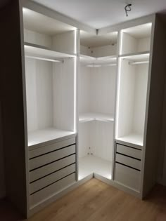 an empty walk in closet with white shelves and lights on the wall above it, along with hardwood flooring