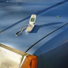 an old cell phone laying on the hood of a blue car with it's tail light turned off