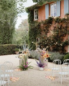 an outdoor wedding venue with white chairs and flowers on the ground in front of a building