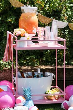 a pink cart with drinks and balloons in the grass