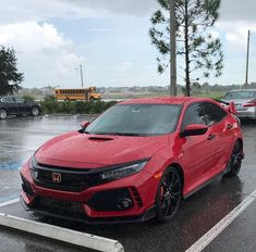 a red car parked in a parking lot next to a school bus on a rainy day