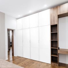 an empty room with white cupboards and wood flooring on one side, wooden shelves on the other