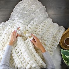 a woman is crocheting a blanket on top of a wooden floor next to a potted plant