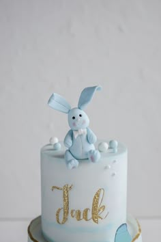 a blue and white cake with a bunny on top that says jack in gold lettering