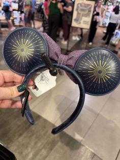 a person holding up a mickey mouse ears headband with fireworks on it at an airport