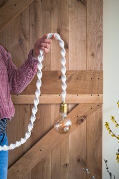 a woman holding a light bulb in her hand and rope wrapped around it to hang on the wall