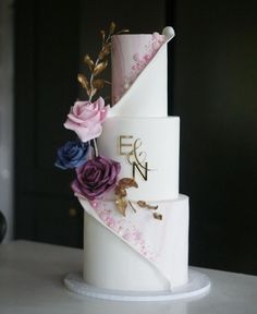 a three tiered wedding cake with flowers on the top and initials on the side