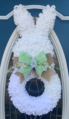 a white wreath with a green bow hanging from the front of a blue door,