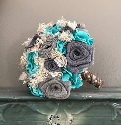 a bridal bouquet with blue and gray flowers on a green table next to a wall