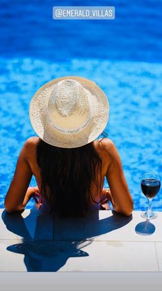 a woman sitting next to a swimming pool with a glass of wine in front of her