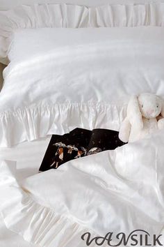 a stuffed animal laying on top of a bed under a white comforter with ruffles