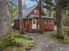 a small red cabin in the woods with trees around it and a flag on the front door