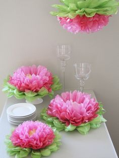 pink and green paper flowers on a table with wine glasses, plates and cups in the background