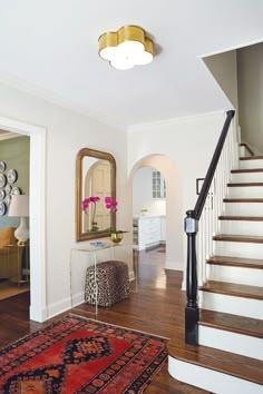 a staircase leading up to a living room with a mirror and rug on the floor