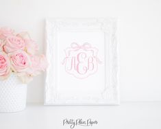 a white vase filled with pink roses next to a framed monogrammed wall art