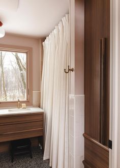 a bathroom with a sink, shower curtain and wood paneled cabinets in it's corner