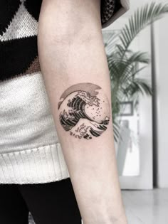 a woman's arm with a black and white wave tattoo on the left forearm