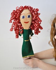 a woman holding a doll with red hair and bows on it's head, in front of a white background