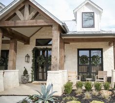 a white house with two wooden chairs on the front porch and plants in pots outside