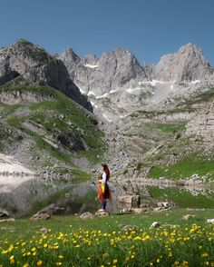 a woman standing on top of a lush green hillside next to a lake and mountains