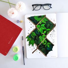 an open notebook with green leaves on it next to some markers and pens, flowers