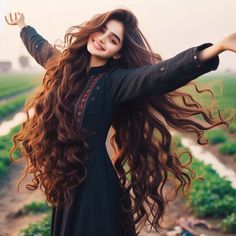 a woman with long brown hair standing in a field holding her arms out to the side