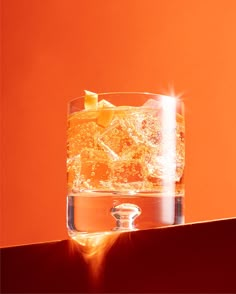 an orange colored background with a glass filled with liquid and ice cubes on the edge