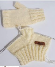 a pair of white knitted mittens sitting on top of a table next to a knitting needle