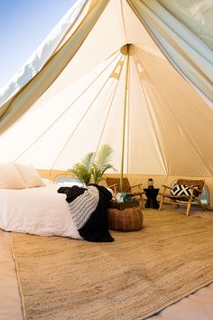 a bed sitting under a white tent next to a wooden bench and table on top of a rug