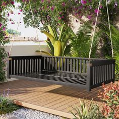 a black wooden bench sitting on top of a wooden deck next to flowers and trees