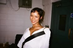 a woman in white shirt and black belt standing next to green door with brick wall