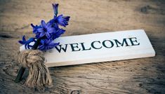 a welcome sign with purple flowers tied to it