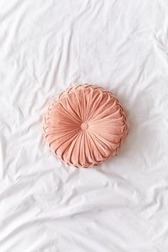 a round pillow sitting on top of a white bed covered in sheets and pillows with pleated edges