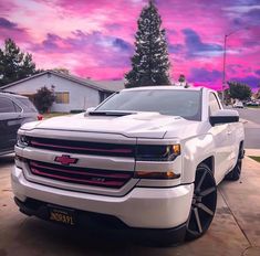 a white truck parked in front of a purple and pink sky with clouds behind it