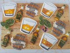 decorated cookies are arranged on a cutting board with alcohol bottles and barrels in the background