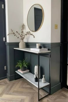 a white and black console table with a mirror on the wall next to potted plants