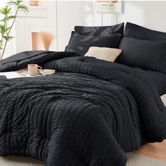 a bed with black comforter and pillows on it in a room next to a potted plant