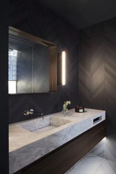 a modern bathroom with marble counter tops and dark wood accents, along with herringbone wallpaper