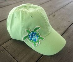 a green hat with a blue turtle embroidered on the front and side, sitting on a wooden surface