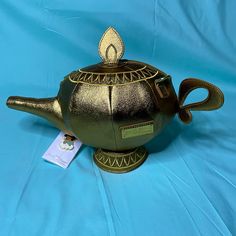 a green teapot with a gold leaf on it's top and a tag attached to the lid