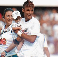 a man holding a baby in his arms while standing next to two women at a baseball game