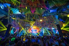 a large group of people standing around in front of a stage with colorful lights on it