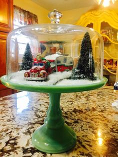 a green cake plate topped with a glass dome filled with snow covered trees and trains