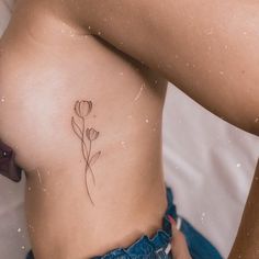 a woman's stomach with a small flower tattoo on her left side ribcage