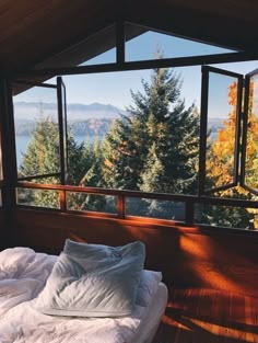 an unmade bed in front of a large window overlooking the trees and mountains outside