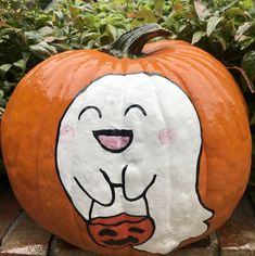 a pumpkin with a ghost face painted on it sitting in front of some shrubbery